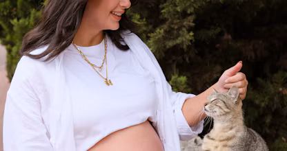 Femeie însărcinată în picioare lângă o pisică